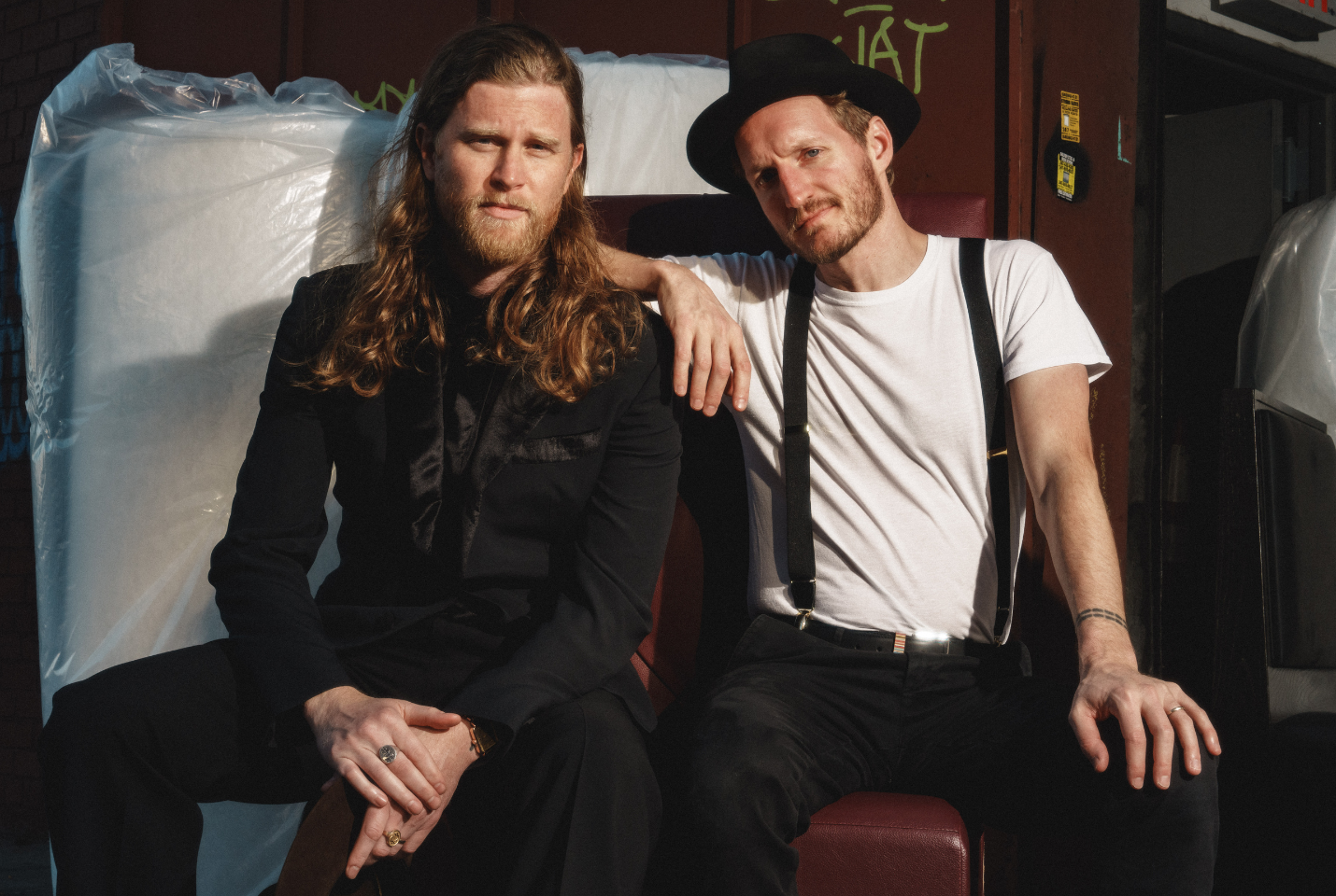 The Lumineers sitting together wearing a suit and a hat and braces 